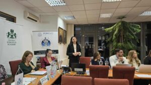 Doktorantka stoi i przemawia do grupy osób