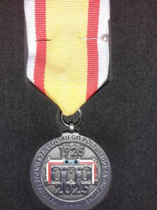 Medal o kształcie okrągłym, srebrny, z napisem: pamięci żołnierza polskiego poległego za ojczyznę 1925-2025, na wstążce w kolorze żółtym z biało-czerwonymi paskami, medal jest przypięty do garnituru w kolorze stalowym