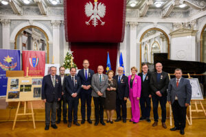 Grupa osób udekorowanych odznaczeniami stoi w Sali Lustrzanej