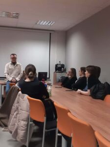 grupa studentów siedzi i słucha mężczyzny prowadzącego wykład