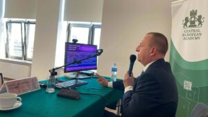 Profesor wygłasza wykład siedząc przy stole w sali konferencyjnej
