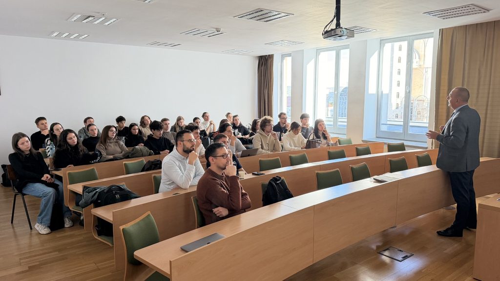 grupa studentów siedzi na wykładzie, mężczyzna wygłasza wykład