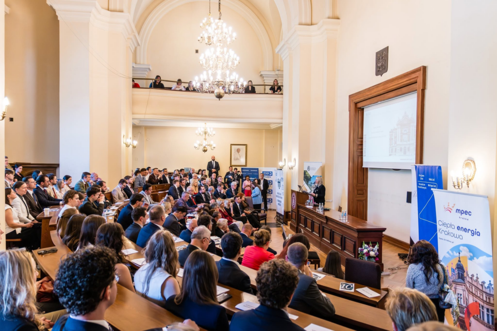 oświetlona aula, w ławkach siedzą osoby słuchające przemówienia