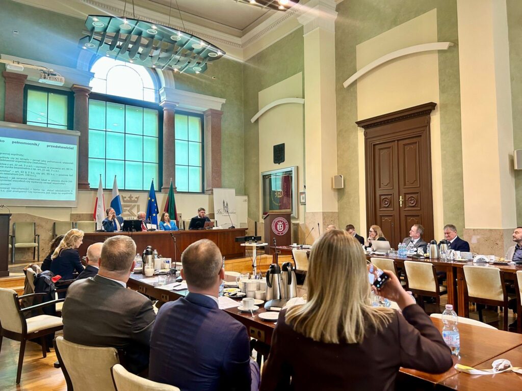 widok sali konferencyjnej, w tle stół konferencyjny i cztery postaci