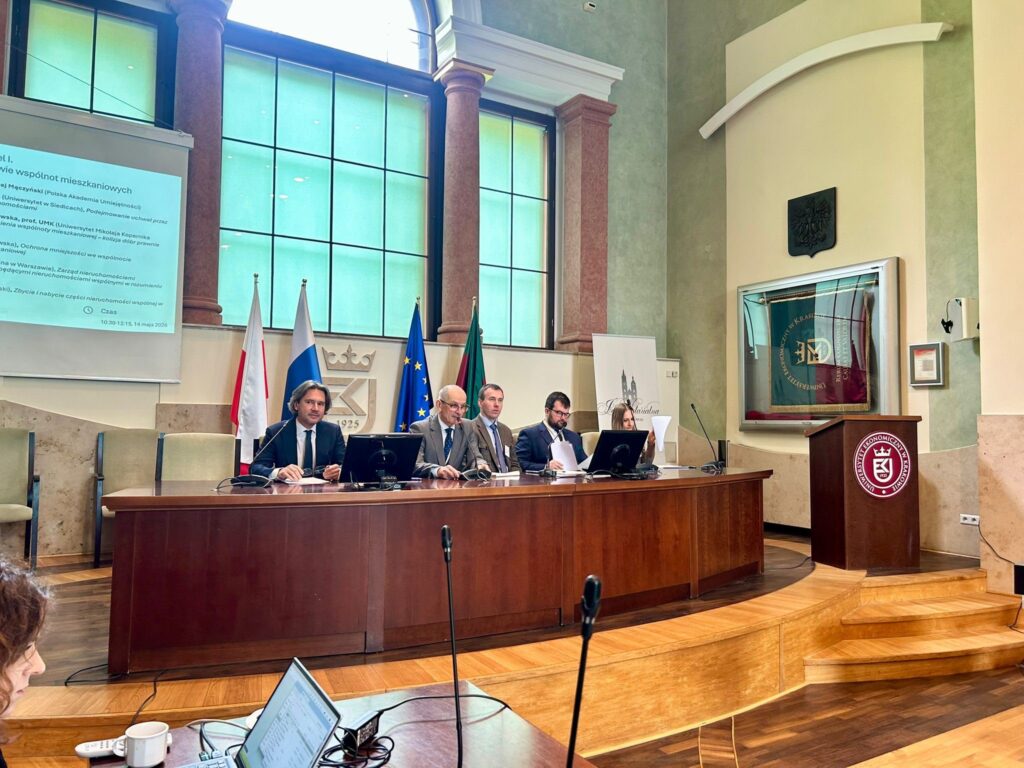 na pierwszym planie osoba z otwartym komputerem, w tle stół konferencyjny i pięć osób przy stole