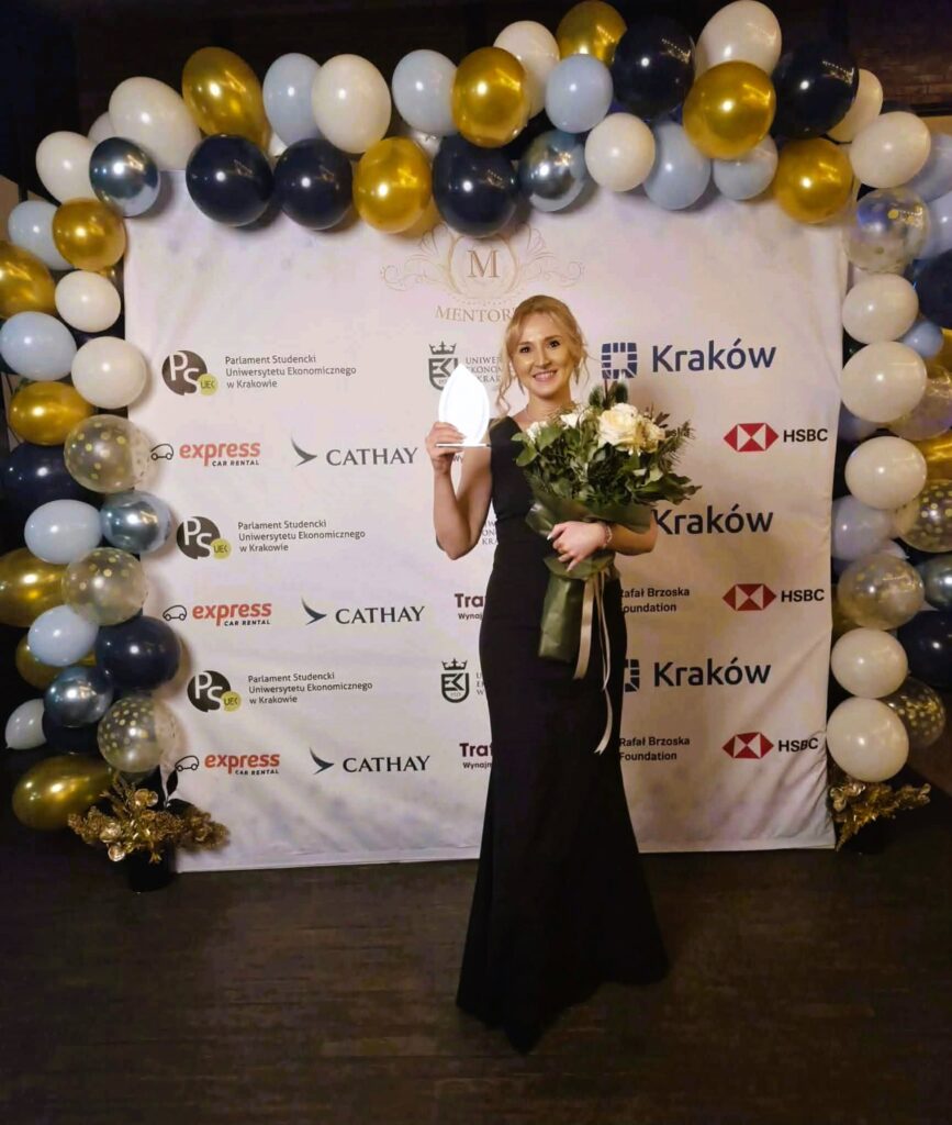 kobieta w czarnej sukni trzyma bukiet kwiatów, dookoła balony,